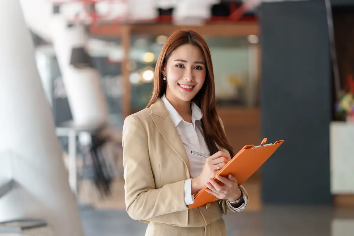 Une femme en costume pantalon prend des notes avec un porte documents