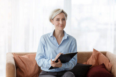 Femme blonde assise sur un canapé avec un porte-bloc à la main
