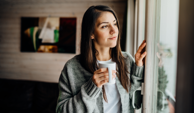 Une jeune femme regarde par la fenêtre en tenant un mug