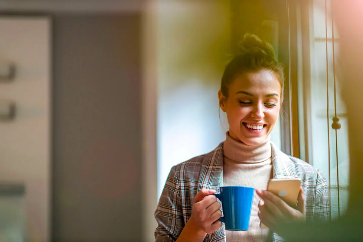 Jeune femme regardant son téléphone avec une tasse à la main