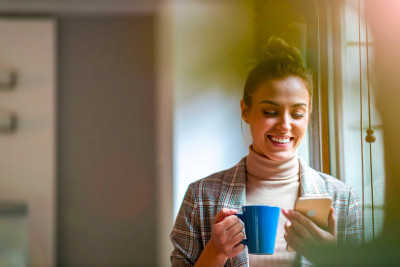 Jeune femme regardant son téléphone avec une tasse à la main