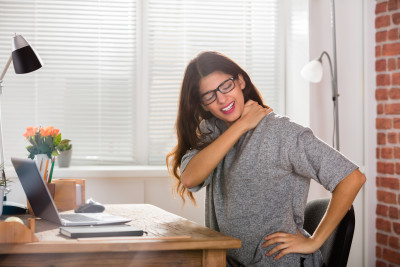 Jeune femme assise à son bureau et souffrant du cou