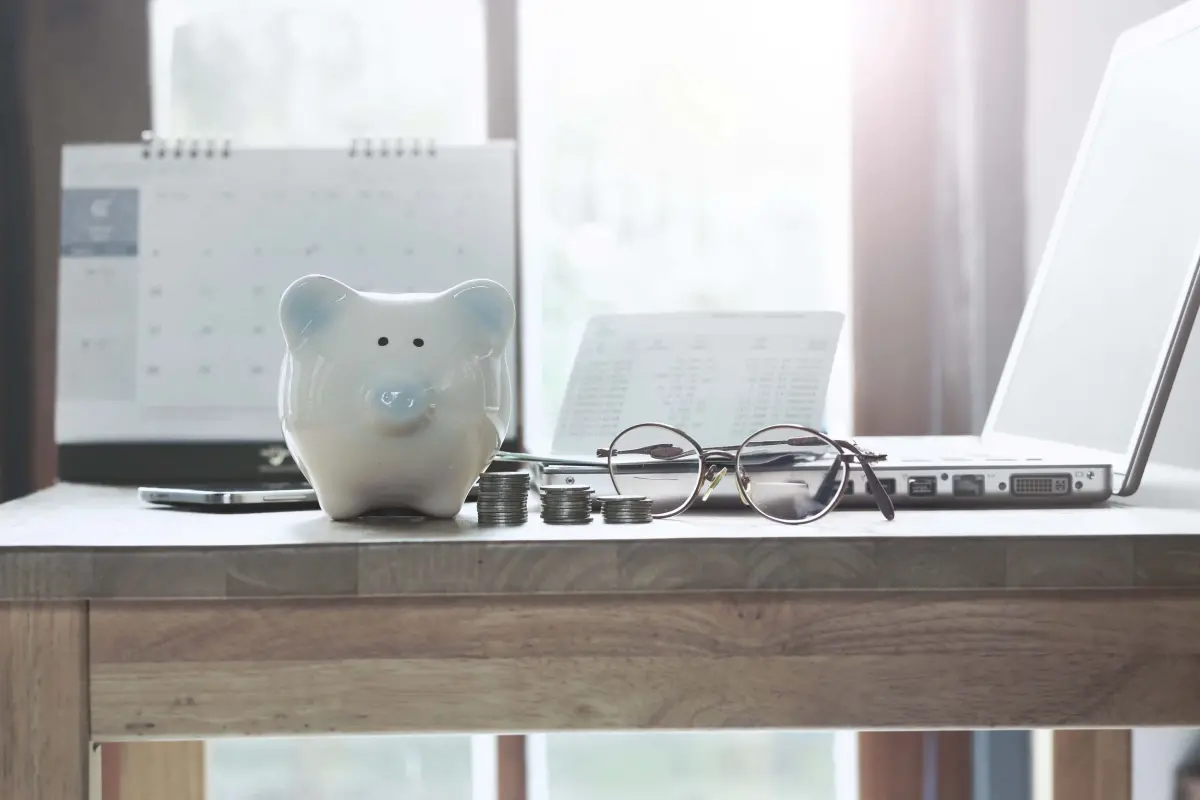 Tirelire cochon avec pièces de monnaie, lunettes et ordinateur posés sur une table